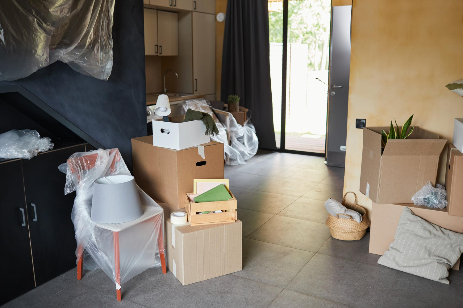 Interior of a room with unpacked moving boxes and wrapped furniture.