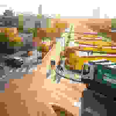 A green garbage truck turns at a serene city intersection, with cyclists and pedestrians enjoying a sunset in a lush urban park.