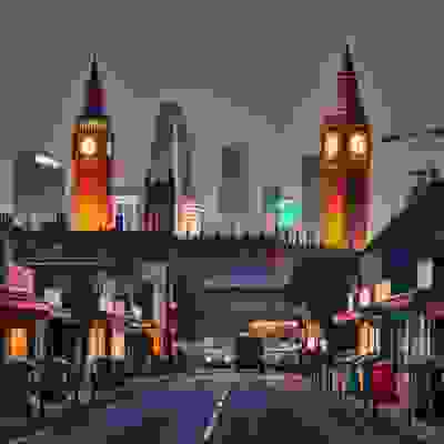 A twilight view of Big Ben surrounded by modern skyscrapers, with a bustling street lined with shops and colorful trash bins.